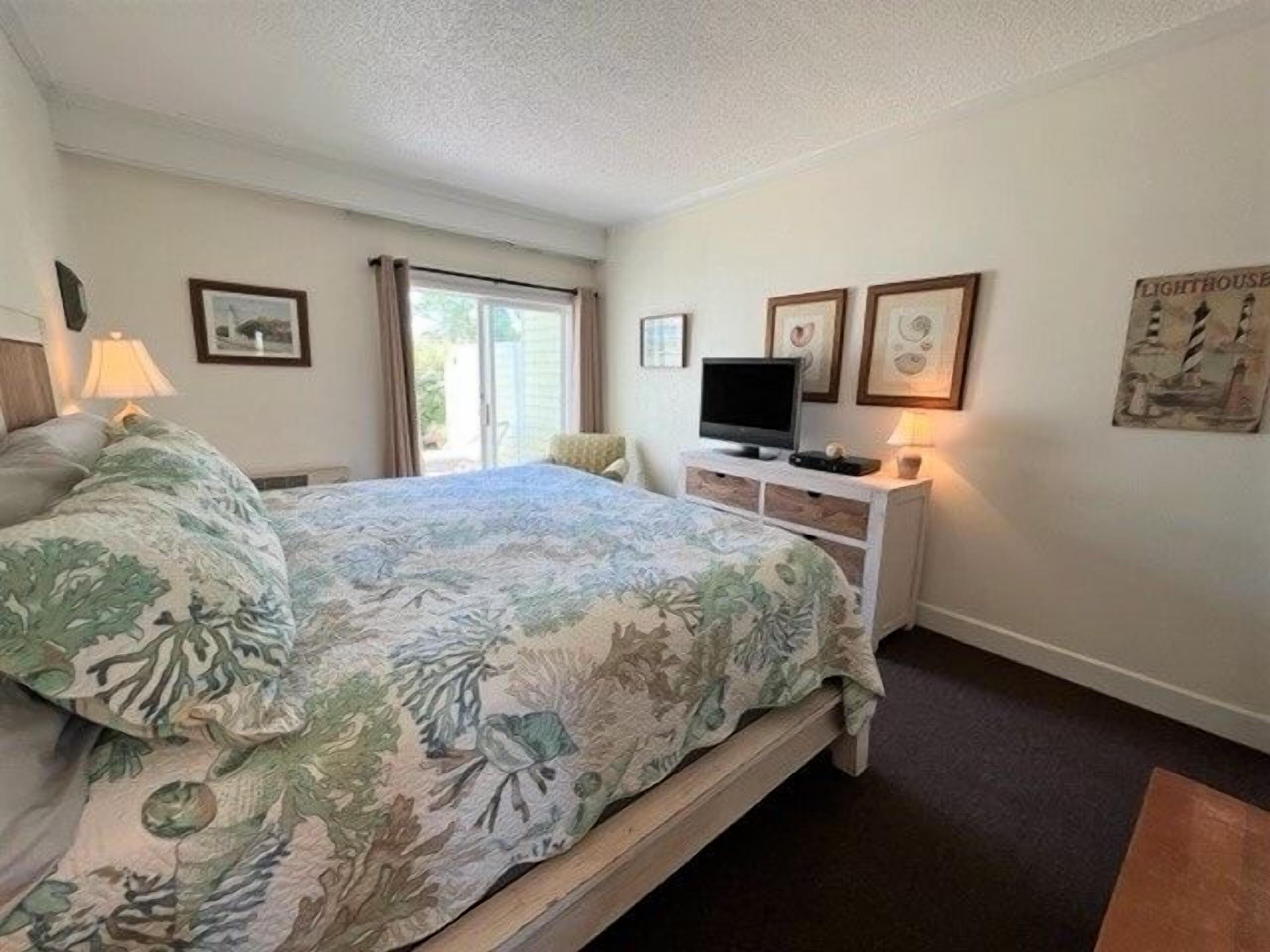 A bedroom with a bed, a television on a stand, a window with curtains, and wall art.