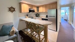 A modern kitchen with wooden cabinets, a central island with bar stools, a stainless steel refrigerator, and a microwave. - Just Beachy!  Short walk to the beach, shops and ferry! (Hatteras)