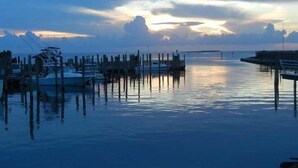 A marina with boats docked at wooden piers, calm water, and a sunset in the background. - Just Beachy!  Short walk to the beach, shops and ferry! (Hatteras)