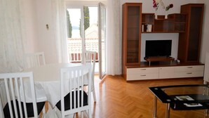 A living room with a TV, wooden cabinets, a glass coffee table, and a white dining table with chairs. - Stunning 2-bed Apartment in Okrug Gornji (Okrug)