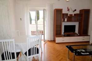 A living room with a TV, wooden cabinets, a glass coffee table, and a white dining table with chairs.