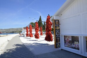 A seaside restaurant with outdoor seating and a menu board advertising pizza, burgers, and fries. - Stunning 2-bed Apartment in Okrug Gornji (Okrug)