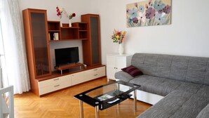 A living room with a grey sofa, a glass coffee table, a TV on a wooden stand, and a painting on the wall. - Stunning 2-bed Apartment in Okrug Gornji (Okrug)