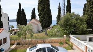 A residential area with a white car parked in the driveway, a stone wall, and a view of the sea and a church in the background. - Stunning 2-bed Apartment in Okrug Gornji (Okrug)
