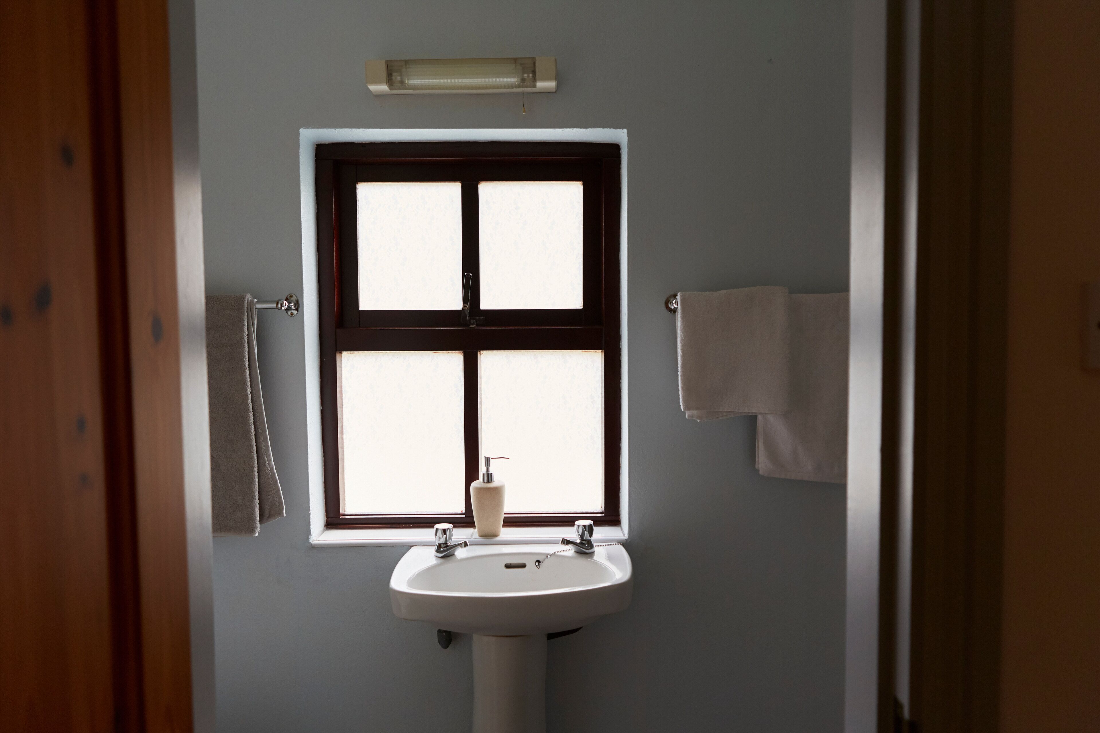 Une salle de bain avec une fenêtre, un lavabo et deux serviettes accrochées au mur.
