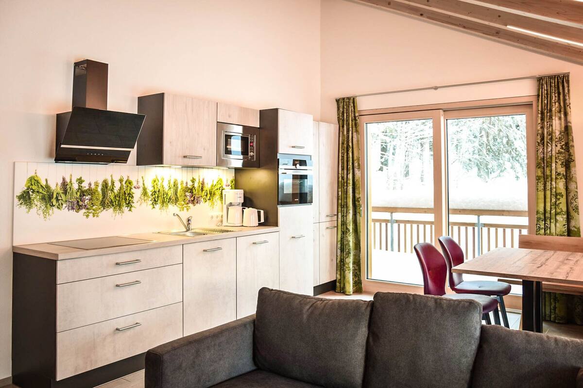 A modern kitchen with a built-in oven, microwave, and a hanging herb display. There is a dining area with a wooden table and red chairs.