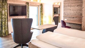Moderni hotellihuone, jossa on suuri sänky, työpöytä ja seinälle asennettu televisio.