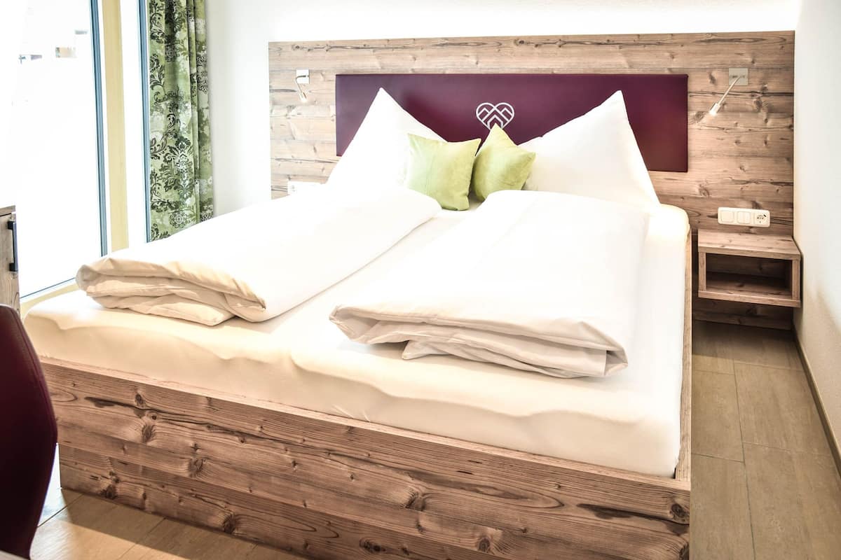 A bed with a wooden headboard, two pillows, and a bedside table with a power outlet.