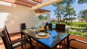 An outdoor dining area with a glass table, wicker chairs, and a pergola overhead. - Beach House (Golf) - Falésia/Albufeira (Olhos Dagua)