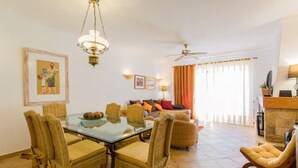 A dining area with a glass table and wicker chairs, a living room with a sofa and cushions, and a ceiling fan. - Beach House (Golf) - Falésia/Albufeira (Olhos Dagua)