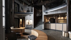 Un vestíbulo amplio con un mostrador de recepción curvo de madera, una escalera y una zona de bar con iluminación colgante.