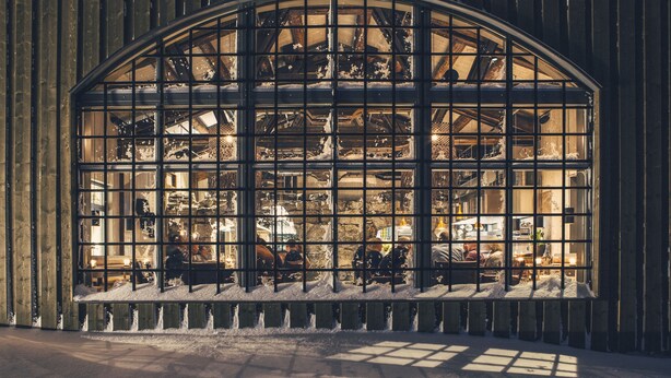 Un amplio ventanal de arco con diseño de cuadrícula, que muestra el interior de un taller con herramientas y equipos.