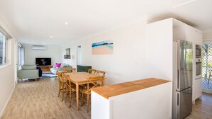 A modern kitchen with a wooden countertop, a stainless steel refrigerator, and a dining area with a wooden table and chairs. - WindanSea Cottage - Pet Friendly - Ocean Glimpses (Vincentia)