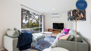 A modern living room with a large window, a flat-screen TV, and a decorative lamp.