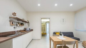 Eine moderne Küche mit Holzarbeitsplatte und eingebauten Geräten, ein Essbereich mit Tisch und Stühlen sowie ein Wohnbereich mit Sofa und einer Uhr an der Wand.