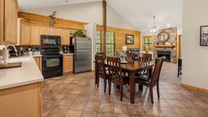 A spacious kitchen with wooden cabinets, a dining area with a table and chairs, and a stone fireplace. - Peaceful Walk-in Cabin with Whirlpool Tub, Gas Fireplace, and Screened-in Porch (Branson)