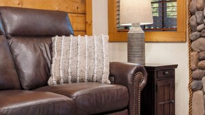 A brown leather sofa with a textured throw pillow, a lamp with a beige lampshade, and a wooden cabinet with a stone wall in the background. - Peaceful Walk-in Cabin with Whirlpool Tub, Gas Fireplace, and Screened-in Porch (Branson)