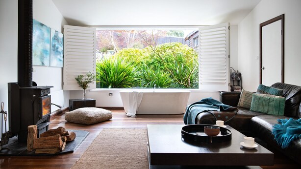 A cozy living room with a large window, a fireplace, a sofa, and a coffee table. - Chestnut Daylesford-Log fire place, spa bath and close to all of Daylesford's attractions (Daylesford)
