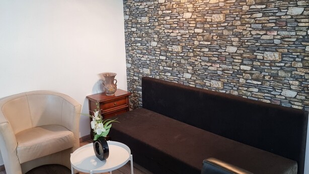 A modern living room with a stone wall, a sofa, a chair, and a small table with a vase. - Relaxhaus Kehl (Kehl)