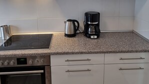 A kitchen with white cabinets, a built-in oven, a stovetop, a kettle, and a coffee maker. - Relaxhaus Kehl (Kehl)
