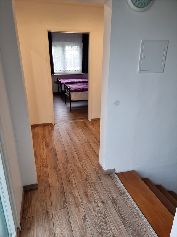 A narrow hallway with wooden flooring leading to a room with two beds and a window with sheer curtains. - Relaxhaus Kehl (Kehl)