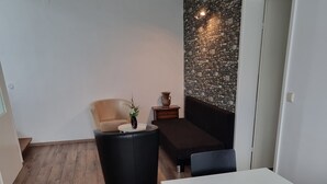 A modern living room with a wooden floor, a white table with decorative vases, a black sofa, and a stone wall. - Relaxhaus Kehl (Kehl)