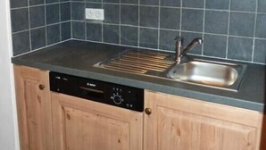 Une cuisine avec des meubles en bois, un dosseret en carreaux noirs et un lave-vaisselle encastré.