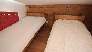 Une petite chambre agréable, dotée de deux lits simples, d’une tête de lit en bois et d’un rideau rouge.