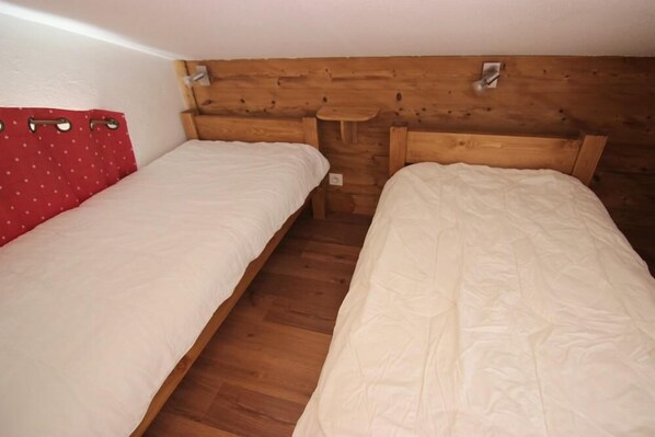 A small, cozy room with two single beds, wooden headboard, and a red curtain. - 150m from ski slopes, 4th floor, view ski slopes, balcony, 60m², Val Thorens (Val Thorens)