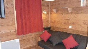 L’intérieur d’un chalet en bois, avec un canapé et des coussins rouges, un rideau rouge et un luminaire blanc au plafond.