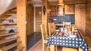 Un intérieur en bois comprenant une table à manger pour quatre personnes, un escalier et un coin cuisine.