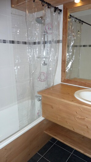 Een badkamer met een houten wastafelmeubel, een witte wastafel, een douchegordijn en een betegelde douche.