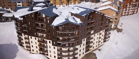 Un hôtel à plusieurs étages, doté de balcons et d’un toit enneigé, entouré d’autres bâtiments.