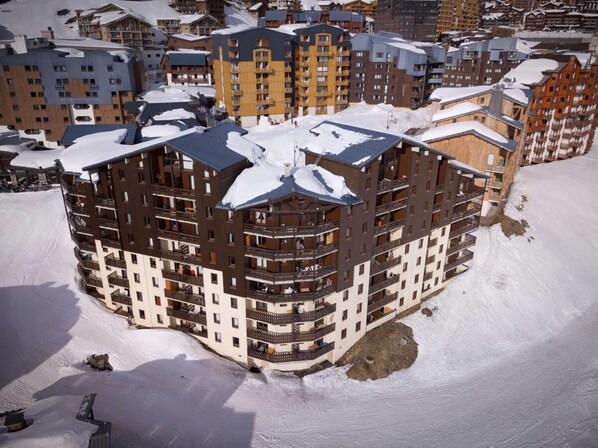 Un hôtel à plusieurs étages, doté de balcons et d’un toit enneigé, entouré d’autres bâtiments.