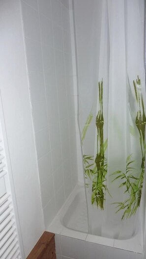 A bathroom with white tiled walls, a shower with a bamboo-themed shower curtain, and a wooden bench. - 150m from ski slopes, 4th floor, view ski slopes, balcony, 60m², Val Thorens (Val Thorens)