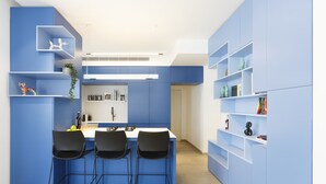 A modern kitchen with blue cabinetry, a white countertop, and three black bar stools. - AirTLV - Nes Tziona Luxury By The Sea (Tel Aviv)
