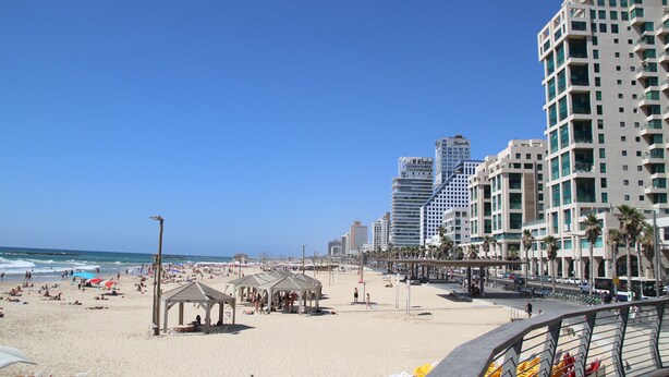 A beach with a pavilion, palm trees, and high-rise buildings in the background. - AirTLV - Nes Tziona Luxury By The Sea (Tel Aviv)