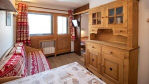 A cozy room with a bed, a wooden cabinet, and a window with curtains. - 50m from resort center, 6th floor, tv, 27m², Val Thorens (Val Thorens)