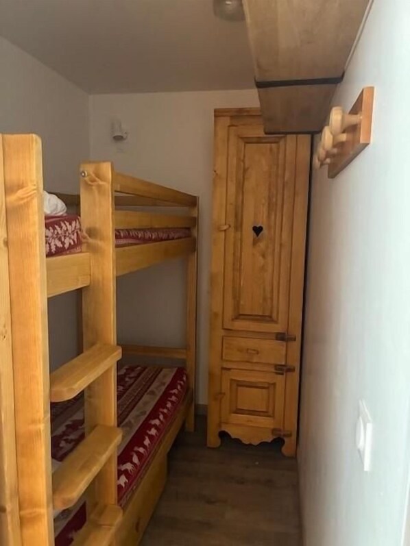 A narrow room with a bunk bed, a wooden wardrobe, and a small shelf.