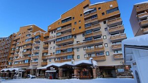 A multi-story hotel with wooden balconies and a ski resort in the foreground. - 50m from resort center, 6th floor, tv, 27m², Val Thorens (Val Thorens)
