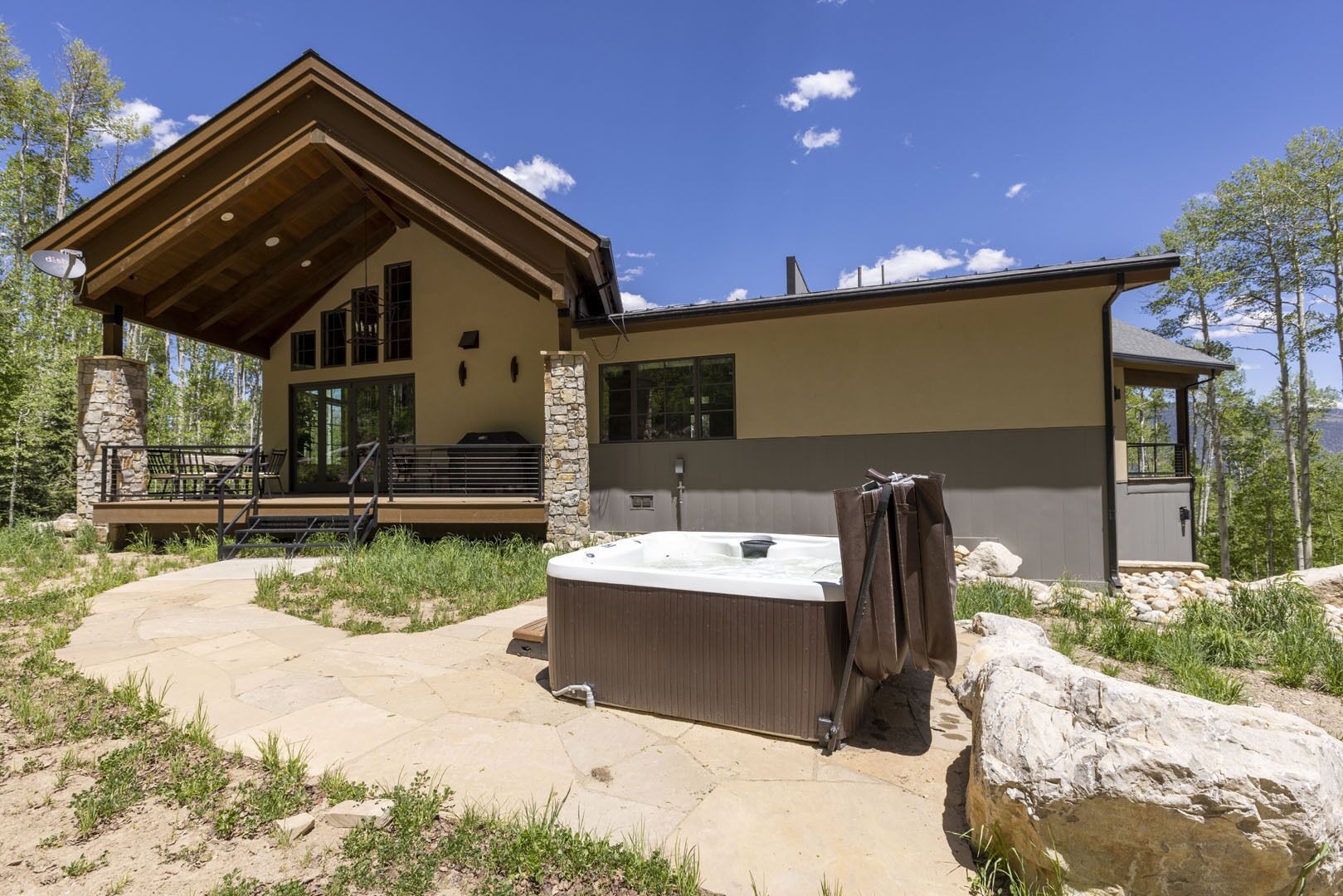 Ein modernes Lodge mit Whirlpool, Steinsäulen und einer Terrasse mit Blick auf eine natürliche Landschaft.