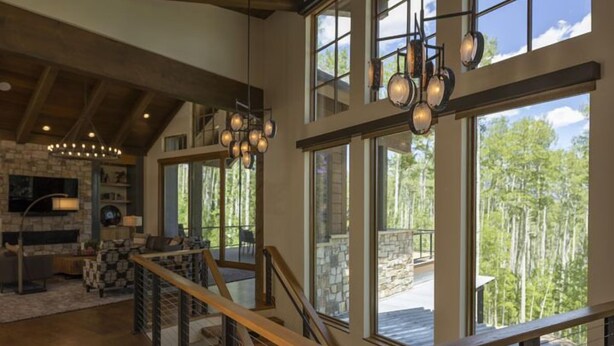 A spacious interior with a wooden staircase, large windows offering a view of the outdoors, and a stone fireplace. - One-of-a-Kind Luxury Home - Hot Tub, Firepit, Views - 8 Min to Purg (Durango)