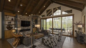 A spacious living room with a stone fireplace, modern furniture, and large windows offering a view of the outdoors. - One-of-a-Kind Luxury Home - Hot Tub, Firepit, Views - 8 Min to Purg (Durango)