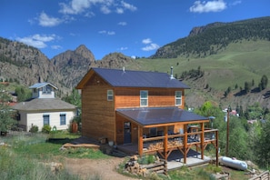 A wooden cabin with a porch, surrounded by a mountainous landscape.