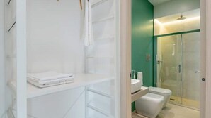 Une salle de bain moderne avec une douche à l’italienne en verre, des éléments d’ameublement blancs et un mur d’accent vert.