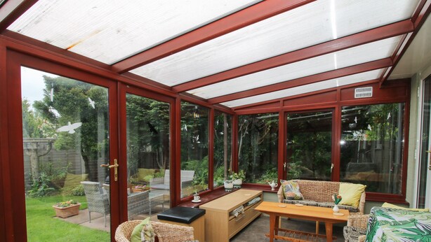 A conservatory with a glass ceiling, wicker furniture, and a view of a garden. - Roseland (Ludlow)