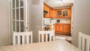 A dining area with a table and chairs, an open door leading to a kitchen with wooden cabinets and appliances. - Roseland (Ludlow)