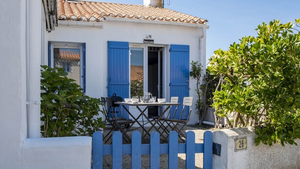 Un edifici blanc amb persianes blaves, una taula amb cadires i una tanca de piquets blaus.