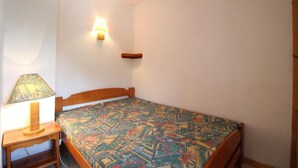 Un dormitorio pequeño y ordenado con una cama individual, una lámpara de noche y una lámpara fijada a la pared.