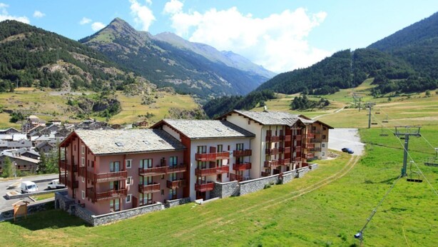 Un refugio de montaña con varios balcones, un telesilla y vistas de montañas circundantes.